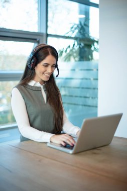 Ofiste dizüstü bilgisayar kullanarak mikrofon danışma müşterisiyle kulaklık takan arkadaş canlısı bayan müşteri destek temsilcisi..