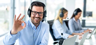 Panoramic view of handsome customer service representative showing approval sign to camera, smiling and gesturing okay at call center. clipart