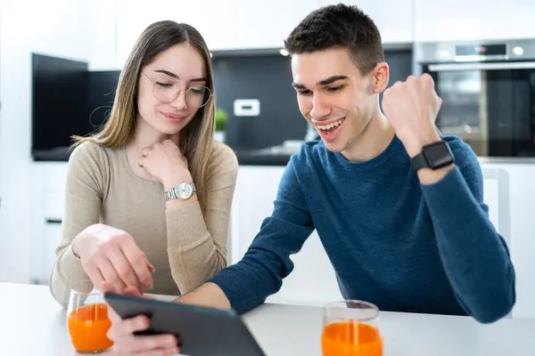 快乐的高中男孩与女友一起在平板电脑上查看测试结果 并在家里举手表决通过考试 — 图库照片