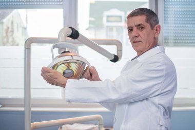 Dostça bir dişçi diş kliniğinde ışık tutan portresi.