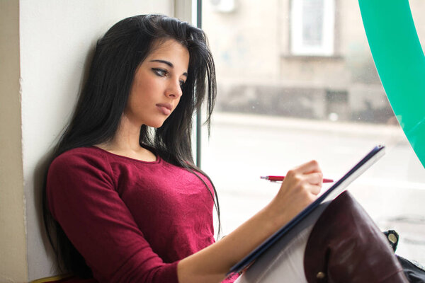 Young women and education, female student studying for college exam near the window.