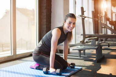 Spor salonunda el ağırlığıyla egzersiz yapan genç bir kadın..