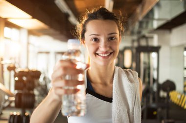 Şişe su içinde jimnastik salonu ile tutan gülümseyen genç kadın