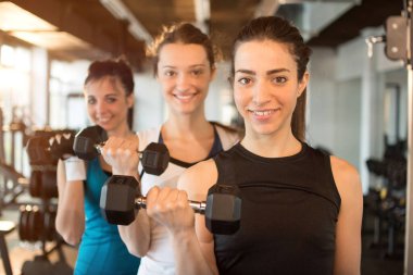 Formda ve formda üç genç kadın spor salonunda ağırlık kaldırıyor. Öndeki ilk kıza odaklan..