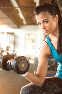 Spor salonunda çelik halteri kaldıran genç bir kadın.