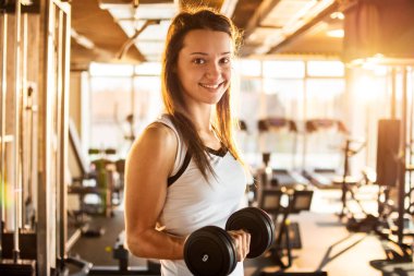 Spor salonunda çelik halteri kaldıran genç bir kadın.