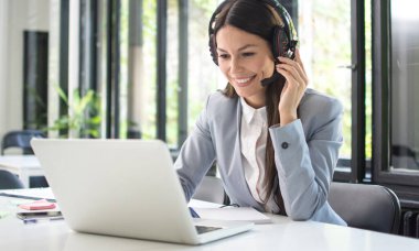 Gülümseyen kadın müşteri destek operatörü müşteriyle konuşuyor ve ofiste dizüstü bilgisayar kullanıyor.