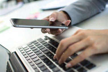 Akıllı telefonu tutan ve dizüstü bilgisayarda yazan kadınların ellerini kapat.