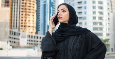 Abaya giyen genç, güzel bir Arap iş kadını sokakta akıllı bir telefonla konuşuyor.