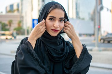 Arap geleneklerine uygun giysiler giyen güzel bir Arap genç kadın. Gülümseyen Arap kadın elleriyle peçe tutuyor.