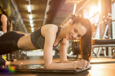 Spor kıyafetli genç bir kadın spor salonunda kalas yapıyor..