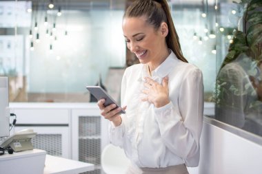 Ofisteki akıllı telefondan iyi haberler okuyan mutlu genç iş kadını.