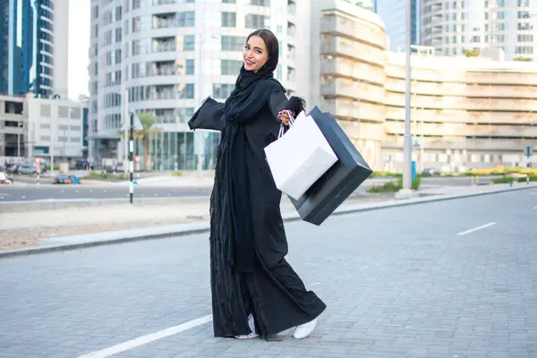 Happy Arab woman in traditional wear holding shopping bags on the city street