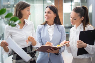 Ofis lobisinde yürürken belgeleri tartışan üç güzel genç iş kadını.