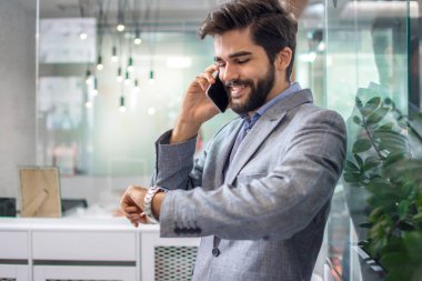 Resmi olarak yakışıklı bir iş adamı cep telefonuyla konuşur ve ofisteki saati kontrol eder.