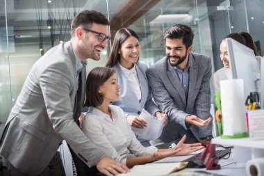 Modern ofiste bilgisayar başında çalışan bir grup neşeli iş adamı.