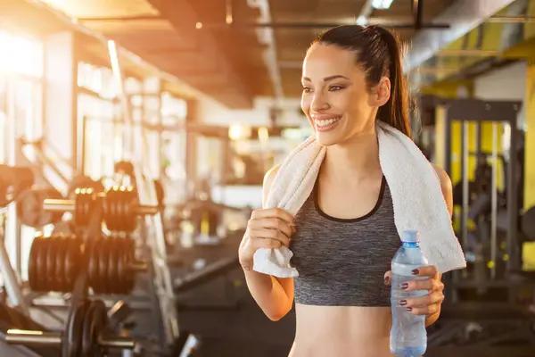 ジムでのスポーツトレーニングのために準備タオルと水ボトルが付いている美しい笑顔の若いフィット感の女性 — ストック写真