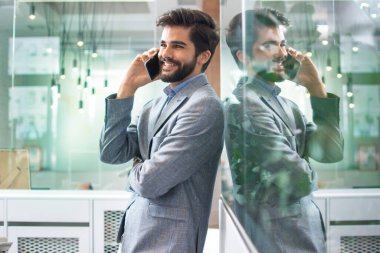 Genç yakışıklı işadamı modern ofiste cep telefonuyla konuşuyor.
