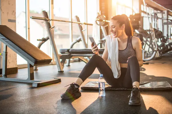 Spor salonunda spor yaptıktan sonra telefonu kullanan neşeli bir kadın..