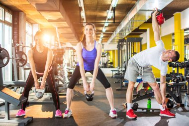 Spor salonunda üç kişilik bir grup kettlebell egzersizi yapıyor.