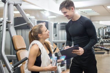 Genç fitness kadını spor salonunda antrenörüyle konuşuyor.