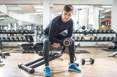 Sportif formda adam spor salonunda ağırlık kaldırıyor.