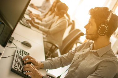 Portrait of handsome male customer service representative, call centre worker, agent, operator, support staff speaking with head set in modern office.