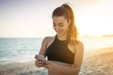 Kumsalda telefonu kullanan gülümseyen sporcu kızın portresi.