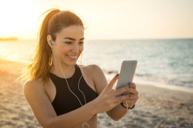 Sahilde cep telefonu kullanan güzel bir kız. Kulaklıklı genç bir kadının portresi açık havada müzik ve mesajlar dinliyor..