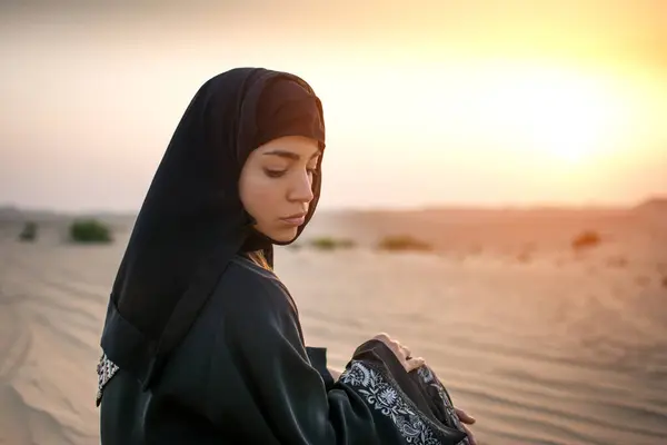 美丽的阿拉伯女子在日落时坐在沙漠中的画像 — 图库照片