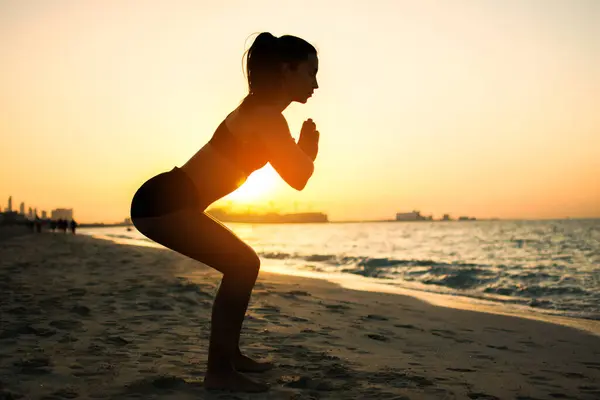 日落时在海滩上做瑜伽运动的漂亮女孩的轮廓 — 图库照片
