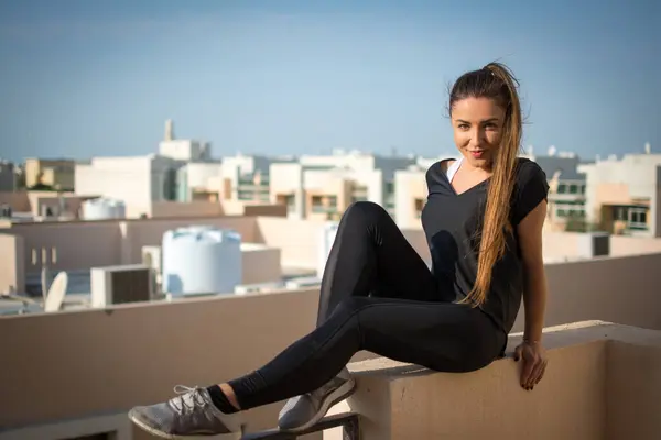 屋上に座っているスポーツウェアで笑顔の若い女性 — ストック写真