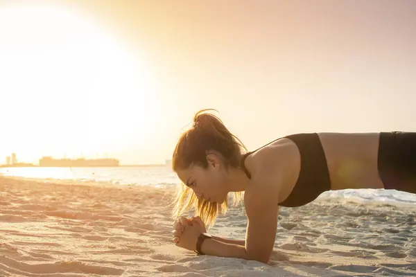 美丽的运动妇女的侧面视图在海滩上的木板位置在日落 — 图库照片