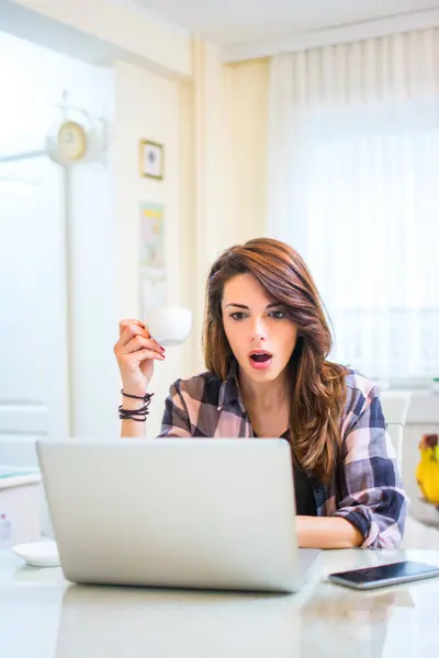 ショックを受けた若い女性がコーヒーカップを持ってノートパソコンを見る — ストック写真