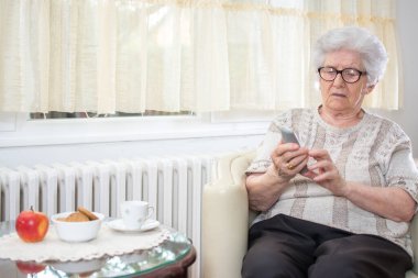 Evdeki koltukta otururken kablosuz telefon kullanan kıdemli bir kadın.