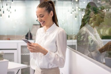 Ofiste cep telefonu kullanan neşeli genç bir iş kadını.