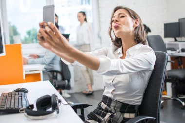 Güzel iş kadını selfie çekiyor, dilini gösteriyor, suratını buruşturuyor ve ofis molasında eğleniyor..