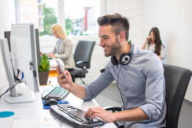 Güzel yakışıklı adam telefon operatörü. Kulaklığı boynunda. Ofiste akıllı telefon kullanıyor.