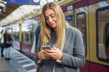 Tren istasyonunda telefon kullanan genç bir kadının portresi.