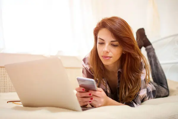 ベッドに横たわりながらスマートフォンを使用する若い女性 — ストック写真
