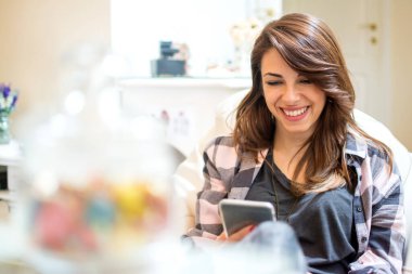 Evde akıllı telefon ve kısa mesaj kullanan genç bir kadın.