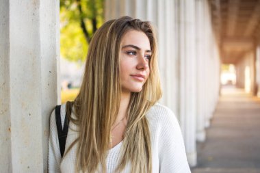 Açık havada sütunlara yaslanan güzel bir kız öğrencinin yakın plan portresi.