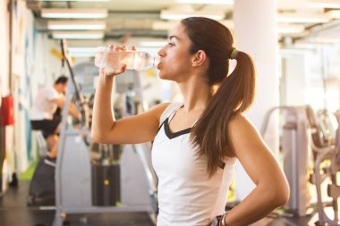 Spor salonunda şişeden su içen genç bir kadının portresi.