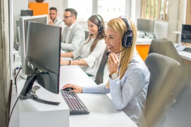 Çağrı merkezi operatörleri. Kulaklıklı genç, güzel bir iş kadını. Ofiste bilgisayarla çalışıyor ve arka planda meslektaşları var..
