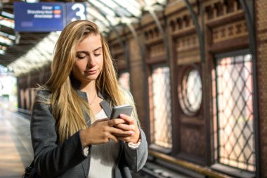 Tren istasyonunda telefon kullanan genç bir kadının portresi.