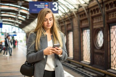 Tren istasyonunda telefon kullanan genç bir kadının portresi.