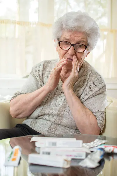 Znepokojená Starší Žena Hledící Přes Stůl Plný Léků — Stock fotografie