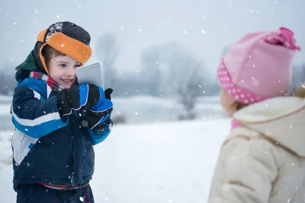 Küçük Çocuk Karlı Kış Gününde Cep Telefonuyla Kız Kardeşinin Fotoğrafını — Stok fotoğraf