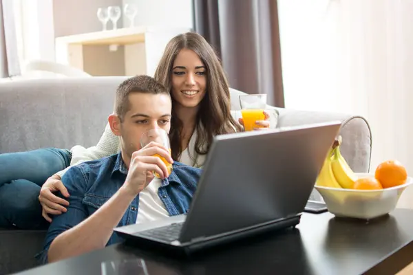 年轻夫妇带着笔记本电脑上网 喝着新鲜的橙汁 — 图库照片