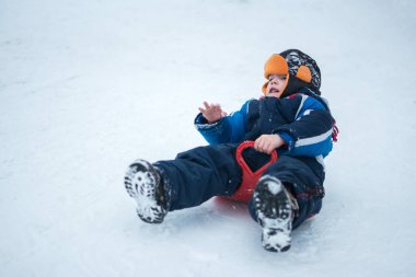 Küçük çocuk dışarıda plastik kızakla geziyor.